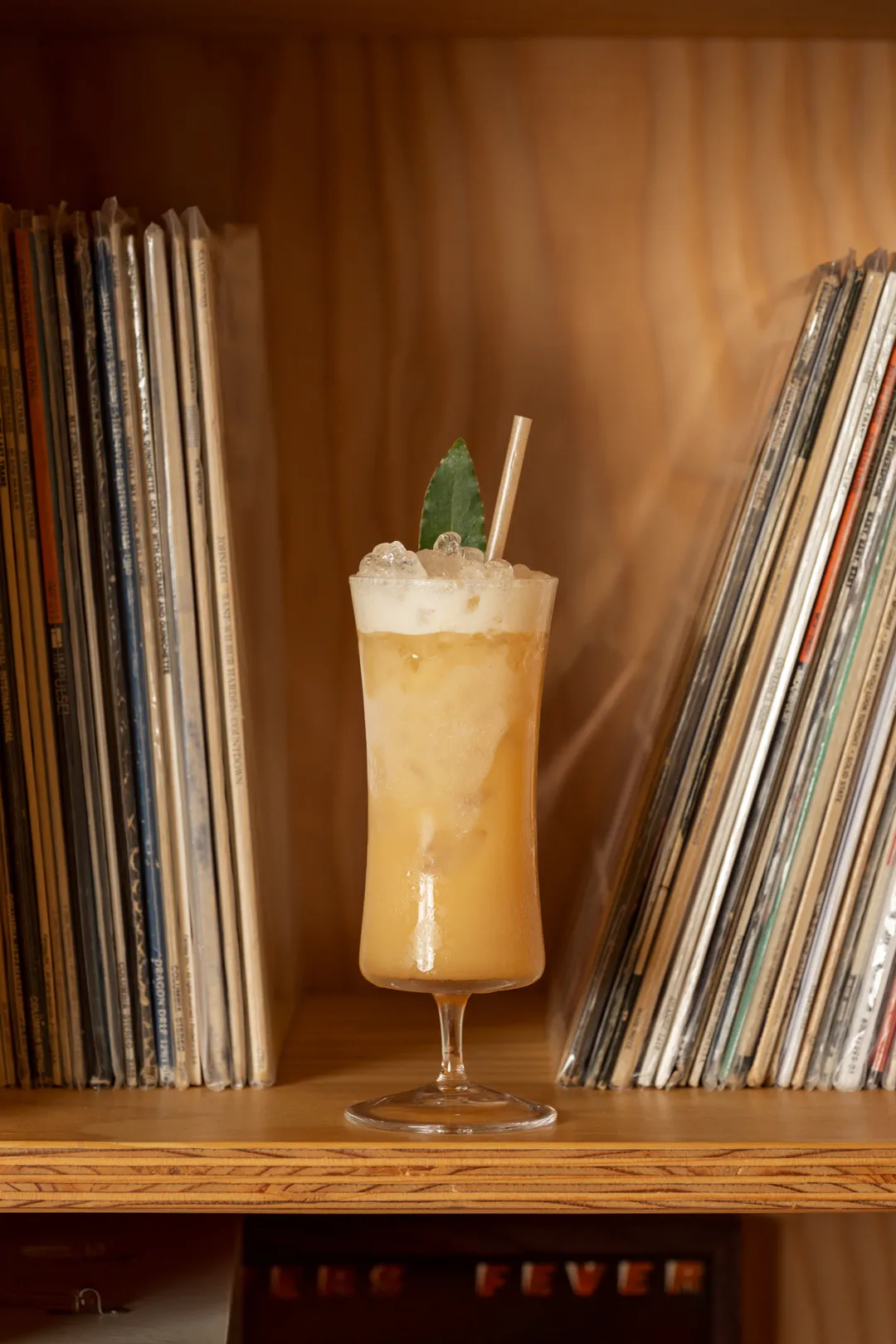 A tall amber cocktail with crushed ice and a bay leaf by the records
