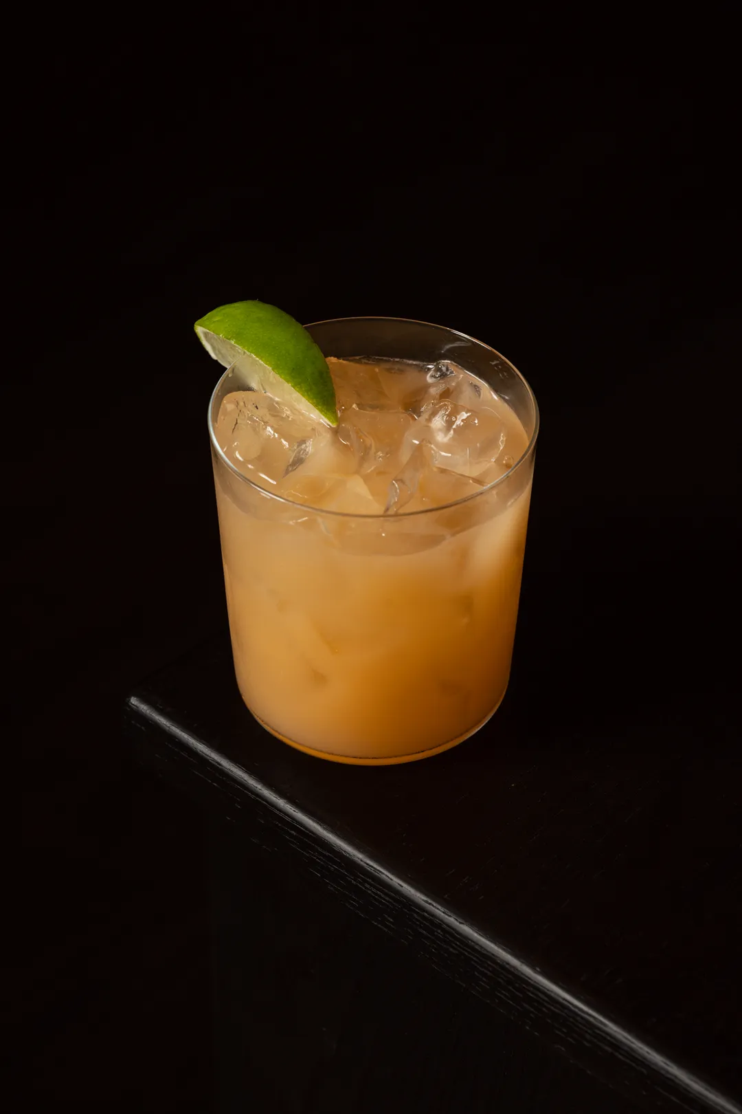 An amber cocktail over ice with a lime wedge