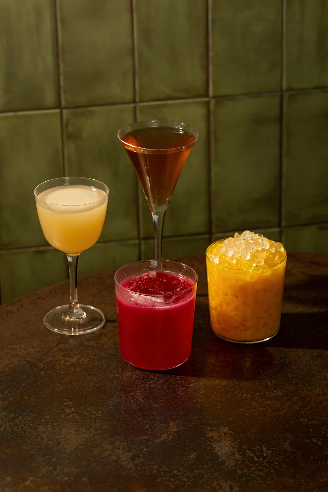 Three cocktails on a rust table against green tile